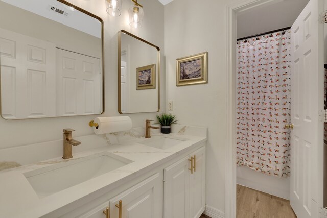 full bathroom featuring a sink, visible vents, double vanity, and wood finished floors