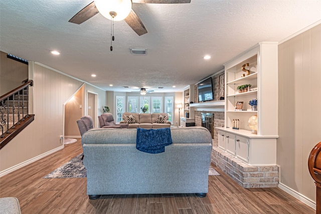 living room featuring a brick fireplace, a ceiling fan, baseboards, visible vents, and stairway