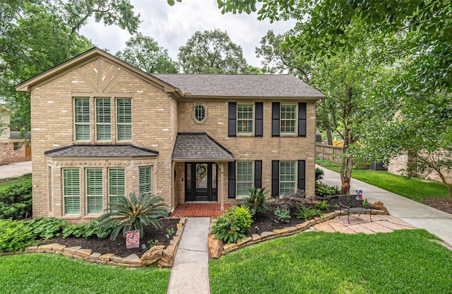 view of front of house featuring brick siding, fence, a shingled roof, and a front lawn