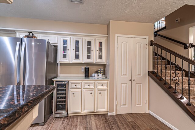 kitchen with wood finished floors, freestanding refrigerator, beverage cooler, glass insert cabinets, and white cabinetry
