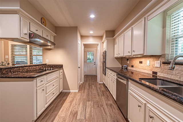 kitchen featuring appliances with stainless steel finishes, a sink, light wood finished floors, under cabinet range hood, and white cabinetry