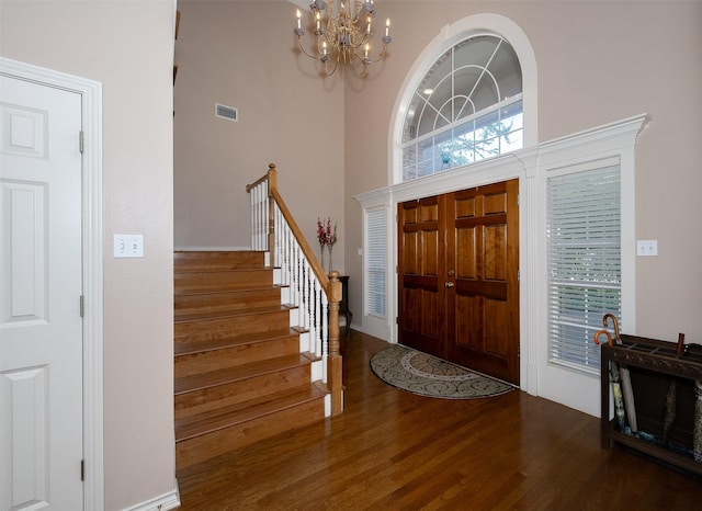entrance foyer featuring an inviting chandelier, stairs, wood finished floors, a towering ceiling, and visible vents