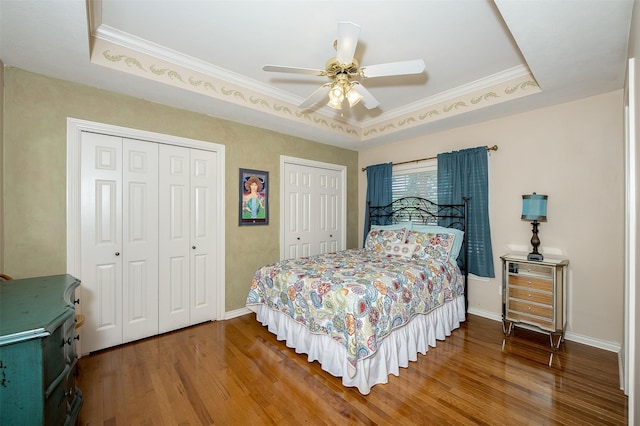 bedroom featuring crown molding, multiple closets, baseboards, and wood finished floors