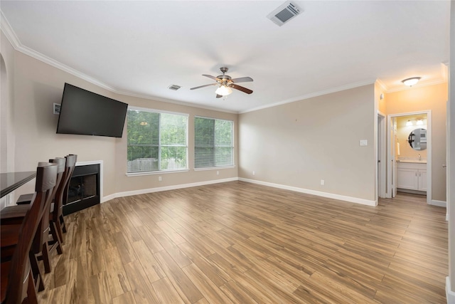 unfurnished living room featuring crown molding, visible vents, baseboards, ceiling fan, and light wood-type flooring