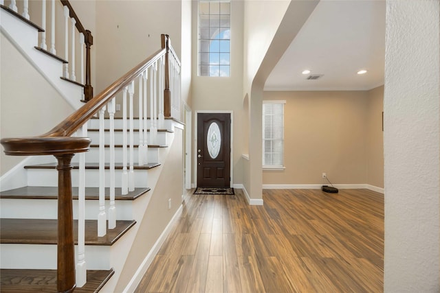 foyer featuring crown molding, arched walkways, baseboards, and wood finished floors