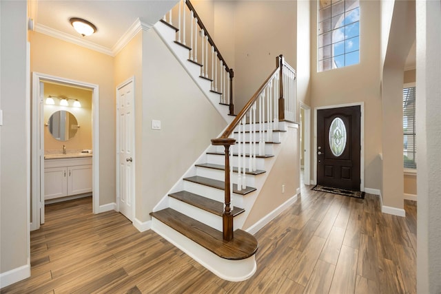 foyer entrance with crown molding, arched walkways, wood finished floors, stairway, and baseboards