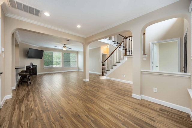 unfurnished living room featuring visible vents, arched walkways, crown molding, and wood finished floors