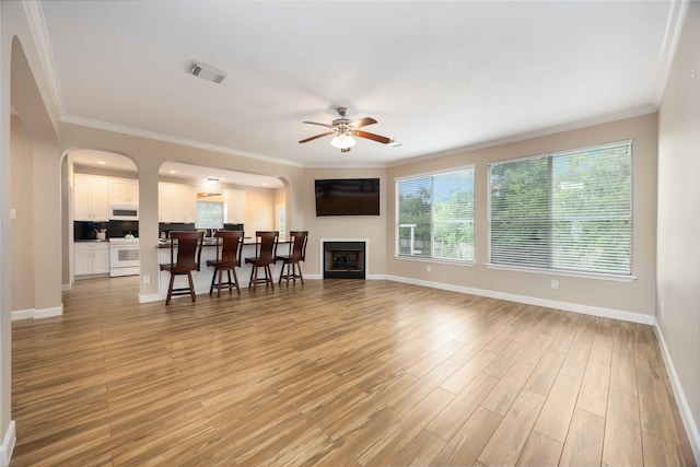 living area with ceiling fan, arched walkways, light wood-style flooring, visible vents, and ornamental molding