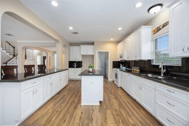 kitchen with a kitchen island, dark countertops, white appliances, arched walkways, and a sink