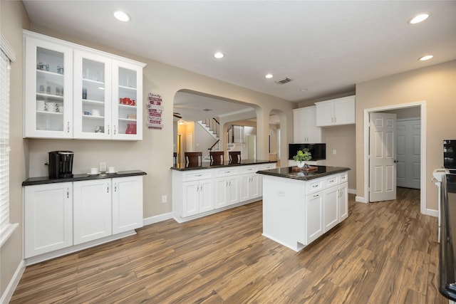 kitchen featuring dark countertops, baseboards, white cabinets, arched walkways, and dark wood finished floors