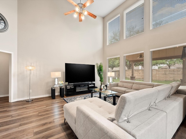 living area with baseboards, a high ceiling, a ceiling fan, and wood finished floors