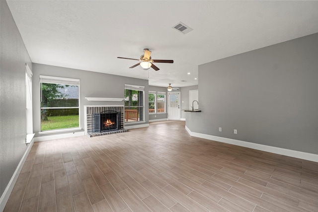 unfurnished living room with visible vents, a brick fireplace, baseboards, ceiling fan, and plenty of natural light