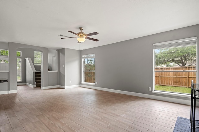 unfurnished living room featuring baseboards, ceiling fan, stairs, and arched walkways