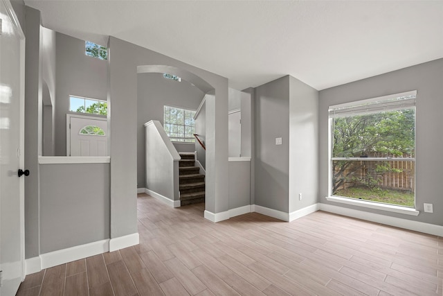spare room featuring stairway, baseboards, arched walkways, and wood finished floors