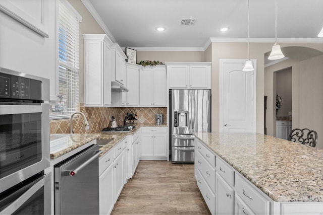 kitchen with white cabinets, stainless steel appliances, a kitchen island, visible vents, and ornamental molding