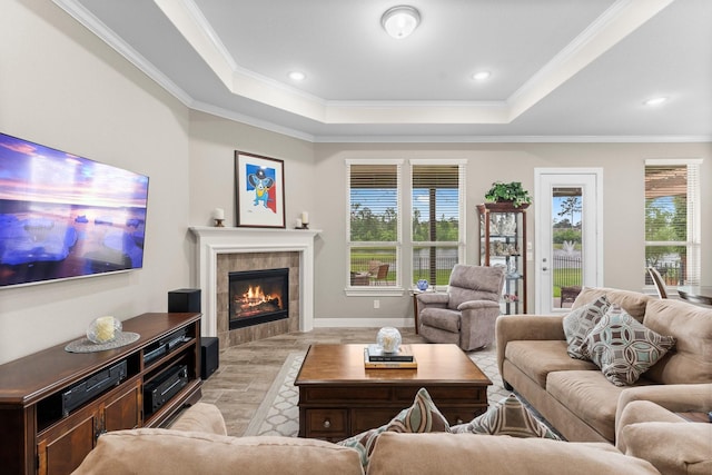 living room featuring crown molding, a tiled fireplace, a raised ceiling, light wood-style floors, and recessed lighting