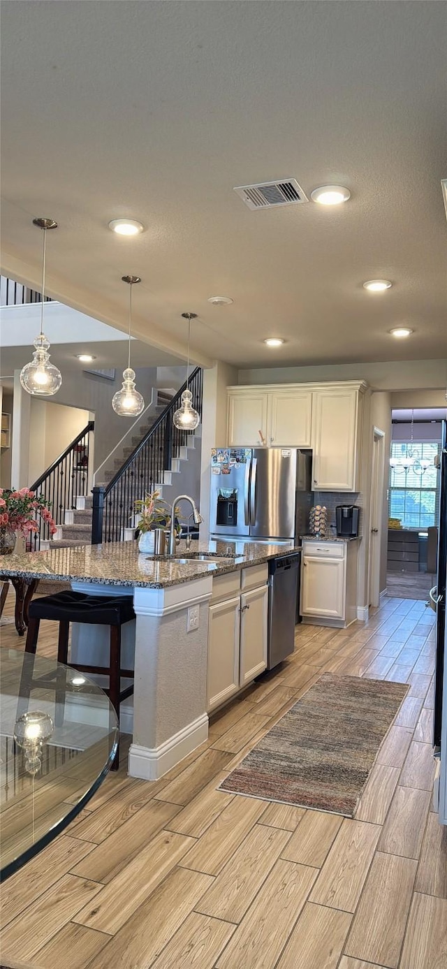 kitchen with wood tiled floor, visible vents, a center island with sink, a sink, and white cabinetry