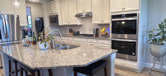 kitchen featuring decorative backsplash, a breakfast bar area, appliances with stainless steel finishes, a sink, and under cabinet range hood