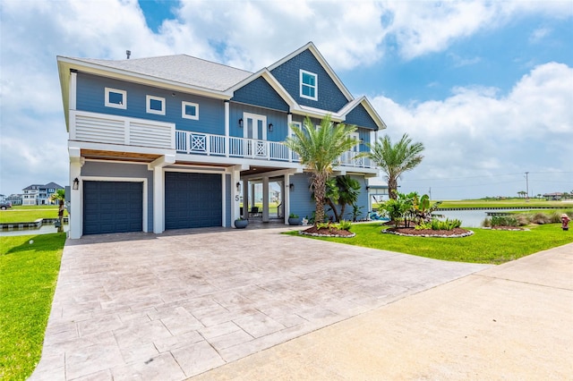 coastal inspired home featuring french doors, decorative driveway, a balcony, a front lawn, and an attached garage