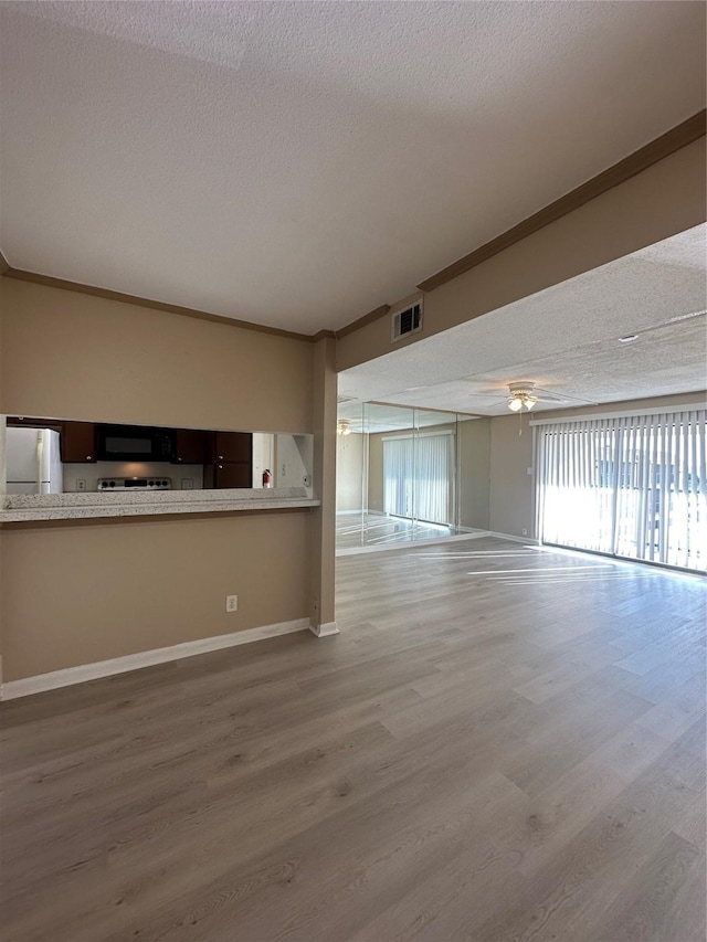 unfurnished living room with visible vents, wood finished floors, baseboards, ceiling fan, and a textured ceiling