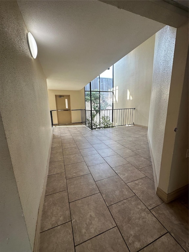 spare room with a textured ceiling, tile patterned flooring, expansive windows, baseboards, and a textured wall