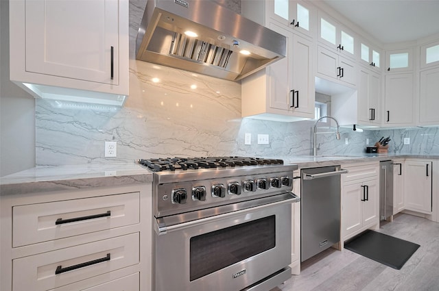 kitchen featuring wall chimney exhaust hood, stainless steel appliances, a sink, light wood-type flooring, and light stone countertops
