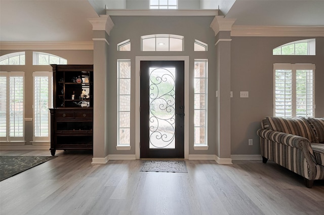 entrance foyer featuring healthy amount of natural light, wood finished floors, baseboards, decorative columns, and crown molding