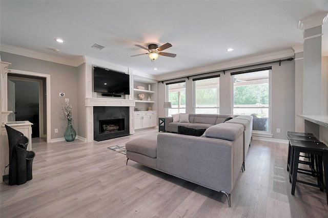 living area with crown molding, ceiling fan, baseboards, light wood finished floors, and a tile fireplace