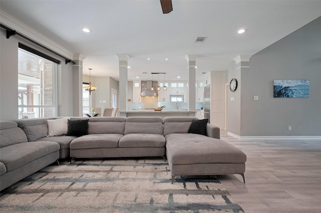 living room featuring ornate columns, light wood finished floors, a chandelier, baseboards, and recessed lighting