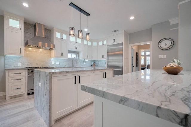 kitchen with wall chimney exhaust hood, high quality appliances, a center island, light stone counters, and backsplash