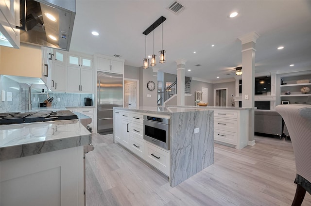 kitchen featuring ornate columns, built in refrigerator, a kitchen island, open floor plan, and light wood-style floors