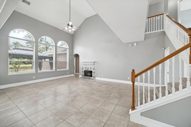 unfurnished living room with tile patterned flooring, high vaulted ceiling, stairway, arched walkways, and a ceiling fan