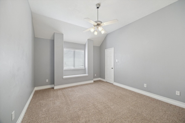 empty room with ceiling fan, light colored carpet, baseboards, and vaulted ceiling