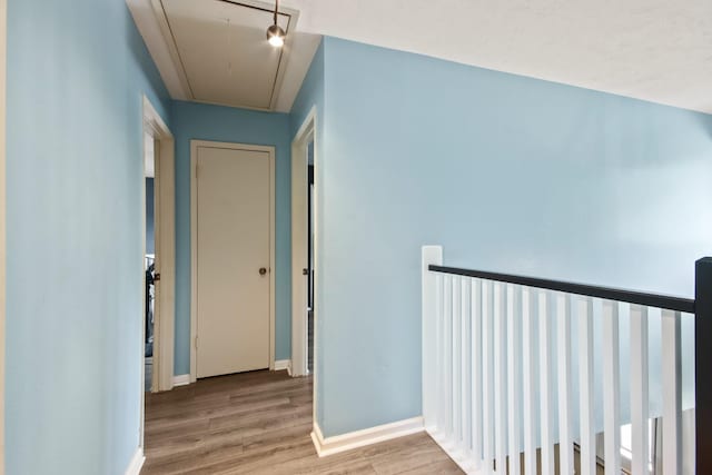 hallway featuring baseboards, wood finished floors, and attic access