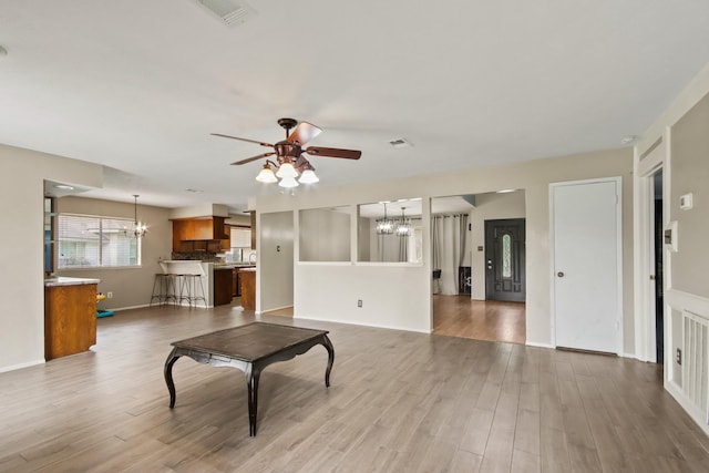 unfurnished living room featuring baseboards, visible vents, wood finished floors, and ceiling fan with notable chandelier