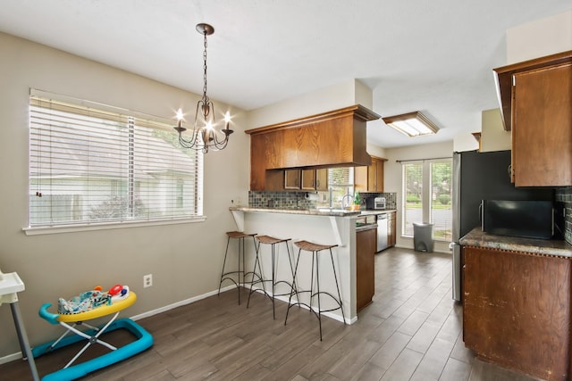kitchen with backsplash, wood finished floors, a peninsula, an inviting chandelier, and a breakfast bar