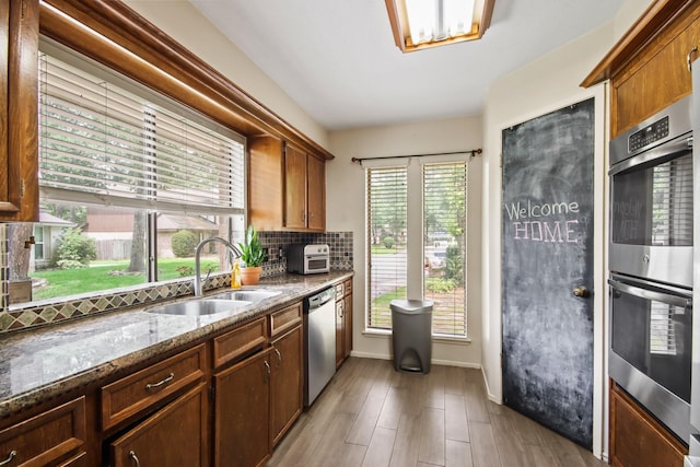 kitchen with appliances with stainless steel finishes, a sink, light wood-style floors, dark stone countertops, and decorative backsplash