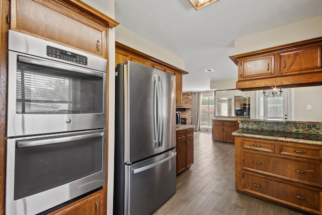 kitchen featuring visible vents, appliances with stainless steel finishes, brown cabinets, wood finished floors, and a notable chandelier