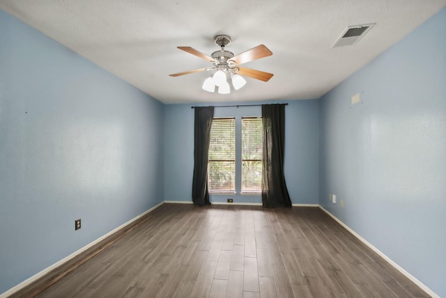 empty room featuring ceiling fan, visible vents, dark wood-style floors, and baseboards