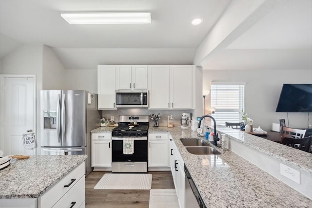kitchen featuring appliances with stainless steel finishes, a sink, white cabinetry, wood finished floors, and vaulted ceiling