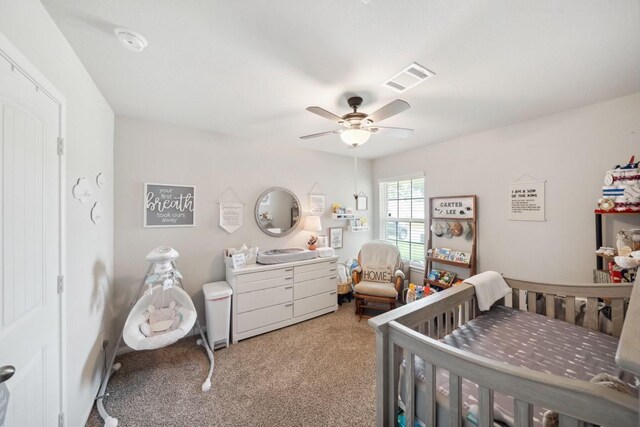 bedroom featuring visible vents, carpet flooring, a crib, and a ceiling fan