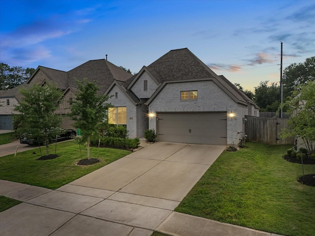 french country home with a lawn, fence, driveway, and brick siding