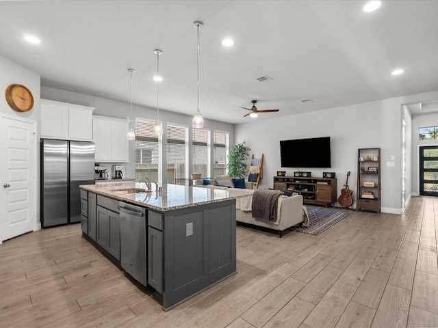 kitchen with gray cabinets, appliances with stainless steel finishes, light stone countertops, a sink, and light wood-style floors