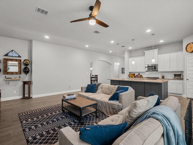 living room featuring visible vents, arched walkways, ceiling fan, and wood finished floors