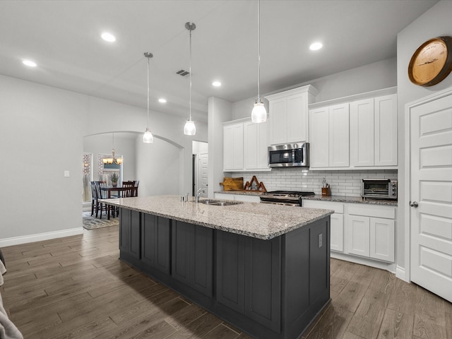 kitchen with white cabinets, appliances with stainless steel finishes, an island with sink, wood finished floors, and backsplash