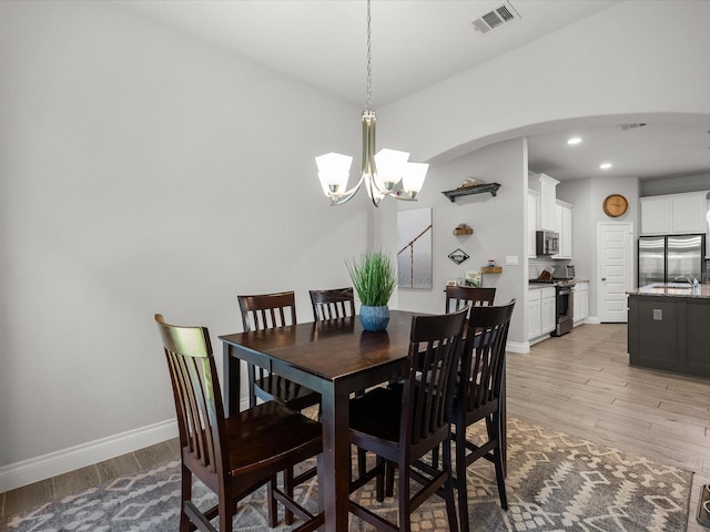 dining room featuring visible vents, an inviting chandelier, light wood-style floors, baseboards, and arched walkways