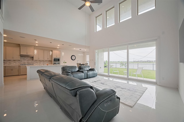 living area with ceiling fan, a towering ceiling, light tile patterned floors, baseboards, and a water view