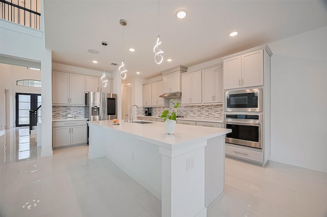 kitchen with decorative backsplash, an island with sink, light countertops, under cabinet range hood, and stainless steel appliances