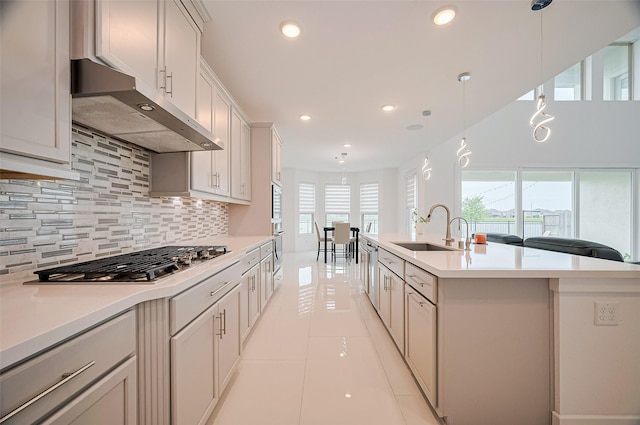 kitchen featuring light countertops, under cabinet range hood, a sink, backsplash, and stainless steel appliances