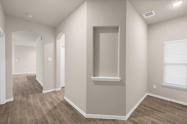 corridor featuring visible vents, arched walkways, dark wood-style flooring, and baseboards